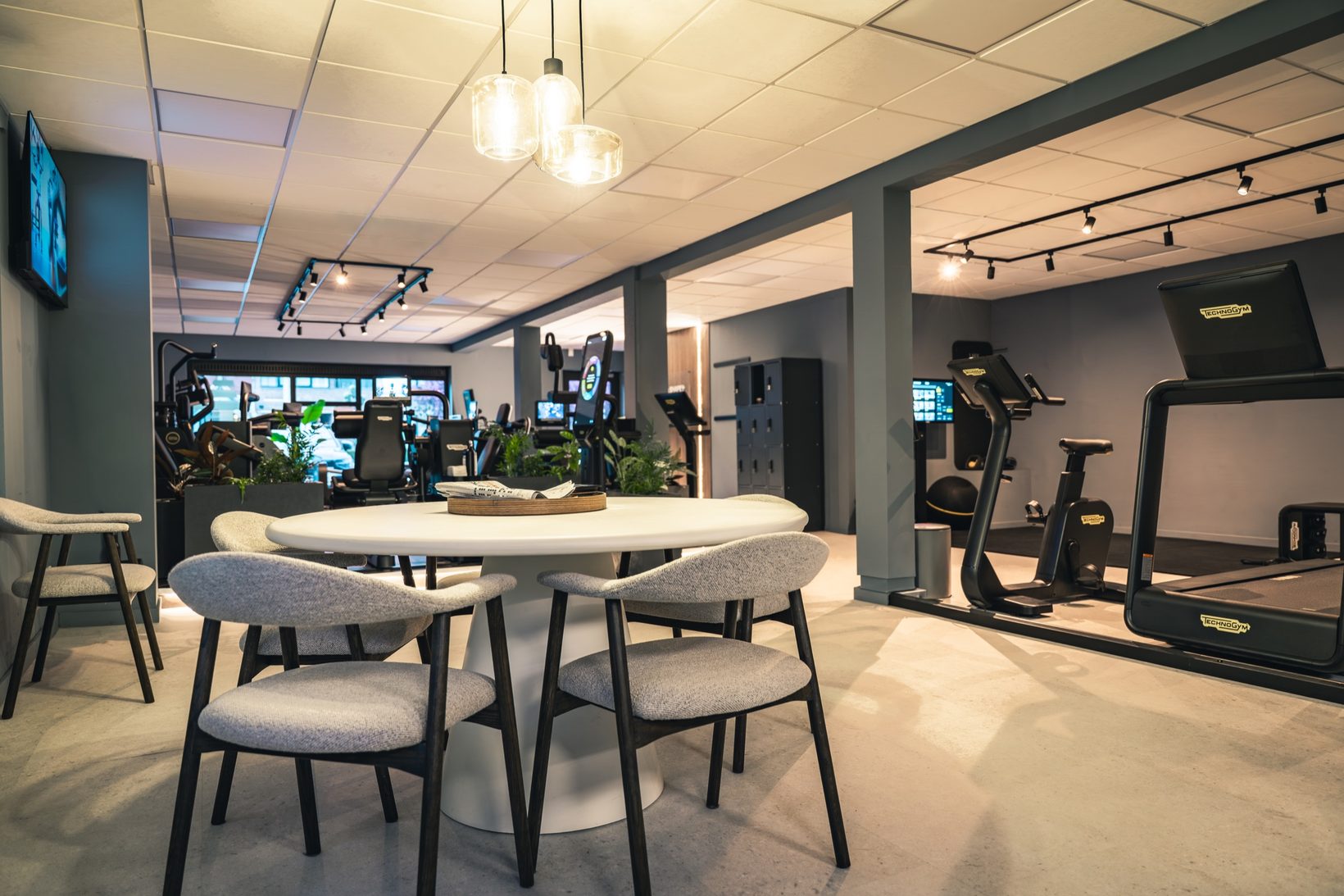 Ontvangstruimte met ronde tafel en zicht op de cardiotoestellen